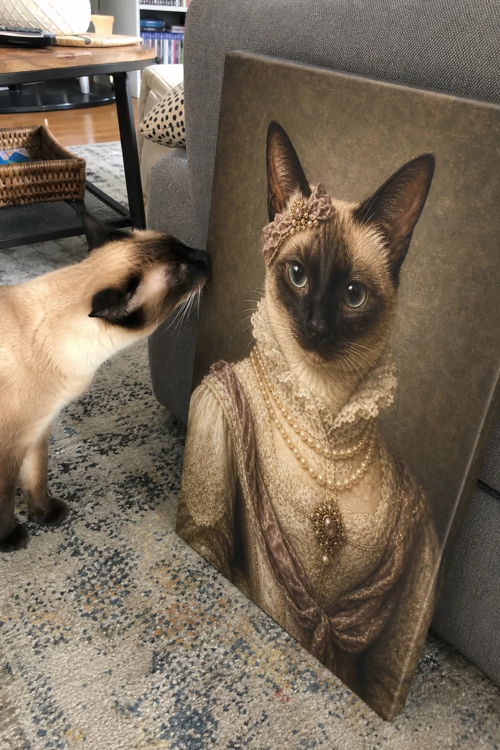 Candid photo of a Siamese cat sniffing a canvas print in a living room. The canvas features a painting of the same cat as an elegant duchess.